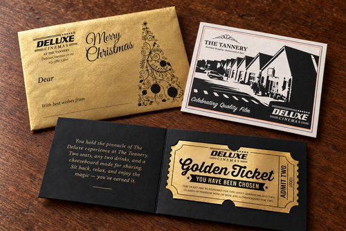 Golden Ticket gift presentation with open black insert, gold envelope and Deluxe Tannery card on a timber table; illustration.